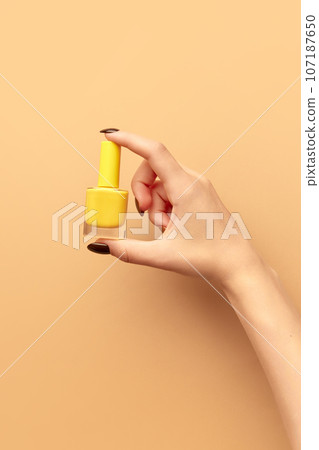 Female hand holding nail polish against beige background. Multicolored pastel manicure. Poster Female hand holding nail polish against beige background. Multicolored pastel manicure. Poster 107187650