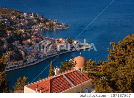 Symi Island, Greece. Greece islands holidays from Rhodos in Aegean Sea. Colorful neoclassical houses in bay of Symi. view of main bay of island, where tourist ferries and yachts moor Symi Island, Greece. Greece islands holidays from Rhodos in Aegean Sea. Colorful neoclassical houses in bay of Symi. view of main bay of island, where tourist ferries and yachts moor 107187867