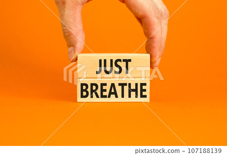 Just breathe and psychological symbol. Concept words Just breathe on beautiful wooden block. Beautiful orange background. Businessman hand. Business psychological and Just breathe concept. Copy space 107188139