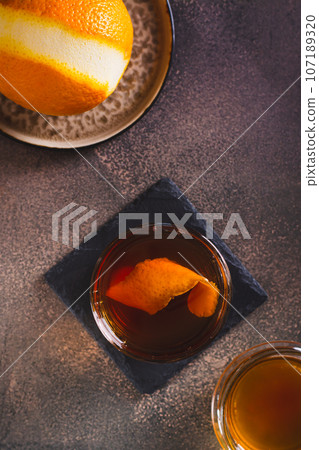Brown butter whiskey cocktail and orange zest in a glass on the table top and vertical view 107189320