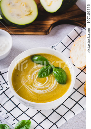 Delicious zucchini soup puree in a bowl and pieces of bread on the table vertical view 107189336