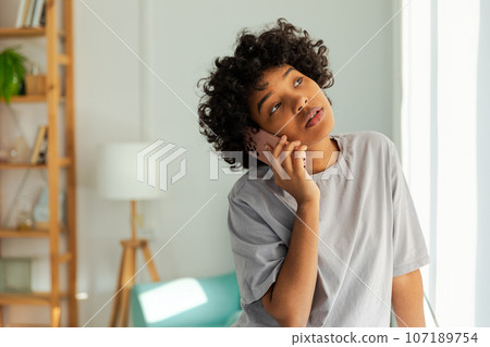 African american girl talking on smartphone at home indoor. Young woman with cell phone chatting with friends. Smiling teen girl making answering call by cellphone. Lady having conversation by mobile 107189754