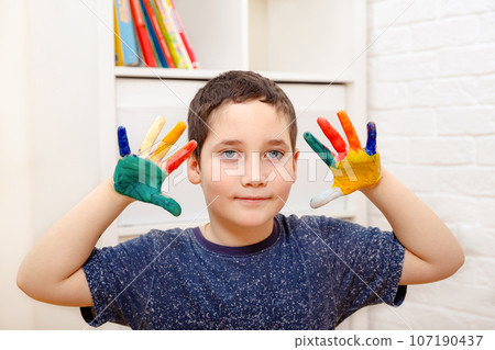 A child with painted colored fingers shows his hands sitting  107190437