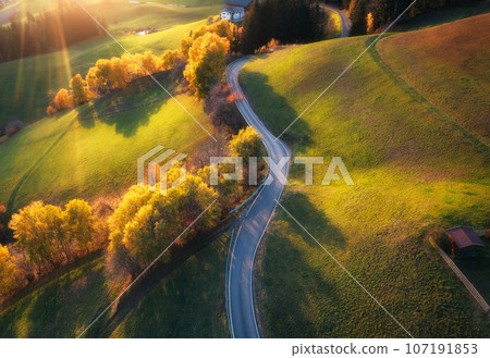 Aerial view of road in alpine meadows and hills at sunset 107191853