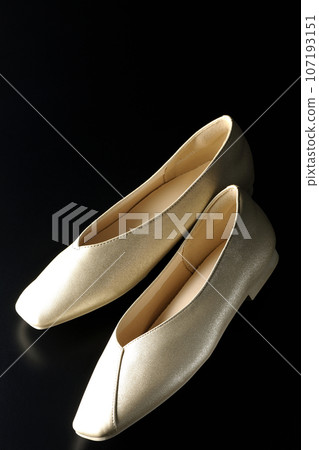 Low-soled gold women's shoes and pumps photographed against a black background Low-soled gold women's shoes and pumps photographed against a black background 107193151