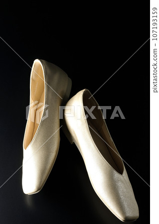 Low-soled gold women's shoes and pumps photographed against a black background 107193159