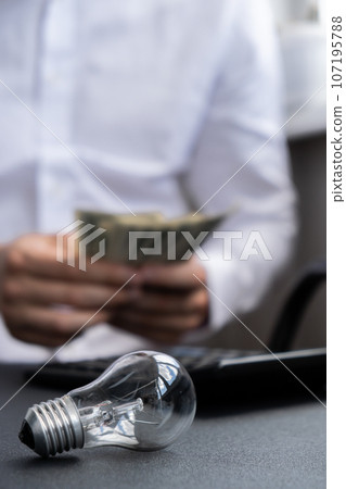 Electric light bulb. Man hands counting expenses bills on electricity banknotes of dollar cash accounting on calculator. Close up of hands unrecognizable Businessman. High prices for energy. Save up 107195788
