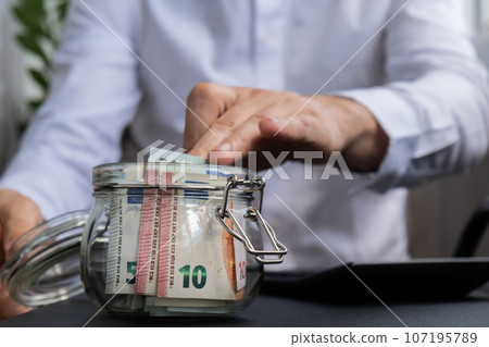 Man hands counting expenses banknotes of euro cash from glass jar in the piggy bank on calculator. Close up of hands unrecognizable Businessman. Save up budget investment concept. Euros fund savings 107195789