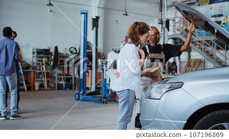 Certified technician in garage workspace fixing car for customer, thoroughly checking underneath vehicle hood. Specialist doing annual maintenance on client automobile in auto repair shop Certified technician in garage workspace fixing car for customer, thoroughly checking underneath vehicle hood. Specialist doing annual maintenance on client automobile in auto repair shop 107196869