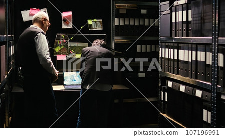 Team of experts connecting clues on board, trying to find all hidden details to solve criminal case and catch suspect. Two police officers working on investigation, clandestine operation. 107196991