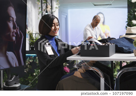 Department center clothing store woman manager putting apparel accessory on display shelf. Boutique asian seller examining tie while managing inventory and checking merchandise in stock 107197090