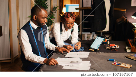 African american tailors picking fabric to create luxury fashion collection with tailoring tools and equipment. Man and woman designers working with materials, handcraft process. African american tailors picking fabric to create luxury fashion collection with tailoring tools and equipment. Man and woman designers working with materials, handcraft process. 107197107