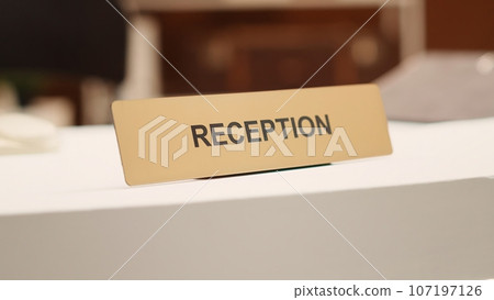 Close up of hotel lobby check in reception plaque sign and folders of tourist accommodation information paperwork. Empty clean desk in stylish resort lounge interior, handheld shot 107197126