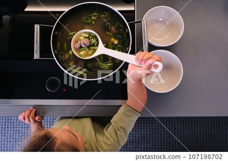 The girl serves the soup with a ladle. The girl serves the soup with a ladle. 107198702