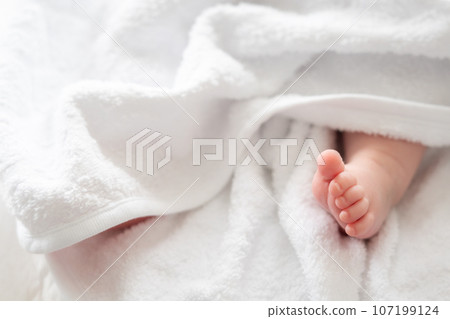 Innocence unveiled: newborn's foot peeking through white softness 107199124