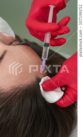 Beauty doctor makes hyaluronic acid rejuvenation beauty injections in head of beautiful young female patient for hair growth and to prevent boldness Beauty doctor makes hyaluronic acid rejuvenation beauty injections in head of beautiful young female patient for hair growth and to prevent boldness 107199252