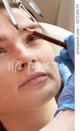 Cosmetologist measures the proportions of the eyebrows with the ruler. 107199274