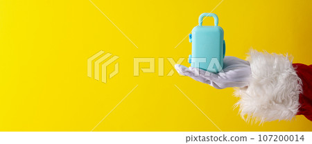 Toy suitcase on Santa's hand on yellow background, space for text 107200014