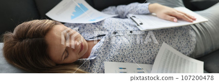 Business woman sleeps on couch with scattered papers from report. 107200478