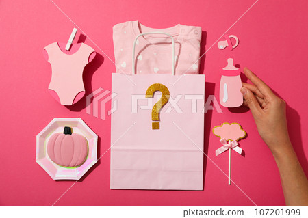Package with baby clothes and paper baby things on pink background, top view 107201999