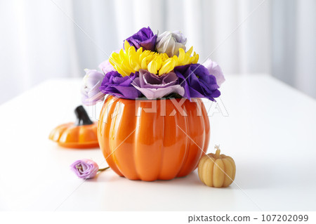 Flowers in pumpkin and candle on light background, close up Flowers in pumpkin and candle on light background, close up 107202099