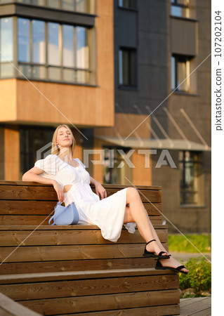 Cheerful woman sitting on bench and enjoying evening sun 107202104