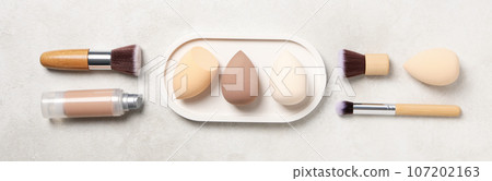 Cosmetic sponges, foundation and brushes on light background, top view 107202163