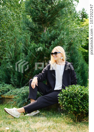 Blonde woman in fleece tracksuit sits in the garden Blonde woman in fleece tracksuit sits in the garden 107202247