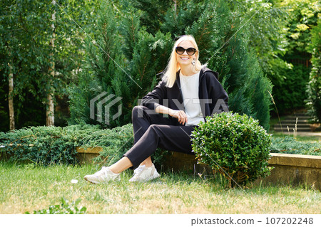 Smiling woman in fleece tracksuit rests in the garden Smiling woman in fleece tracksuit rests in the garden 107202248