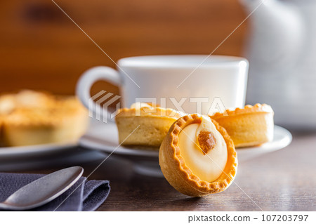 Sweet tarlets. Tasty mini tarts. Mini pie with cream and coffee cup on kitchen table. Sweet tarlets. Tasty mini tarts. Mini pie with cream and coffee cup on kitchen table. 107203797