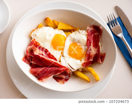 Fried eggs with fried potatoes and sliced cured ham Fried eggs with fried potatoes and sliced cured ham 107204673