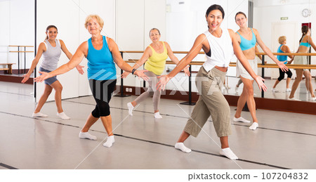 Women practicing vigorous dance movements in group dance class Women practicing vigorous dance movements in group dance class 107204832