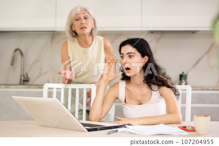 Elderly woman quarrels with young woman working at laptop 107204955