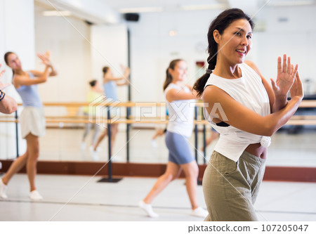 Asian girl dancing modern dance in studio with other dancers Asian girl dancing modern dance in studio with other dancers 107205047