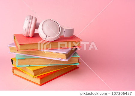 Pink headphones on stack of books on pink background Pink headphones on stack of books on pink background 107206457