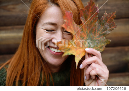 Laughing red-haired middle-aged woman, closed eyes and maple leaf Laughing red-haired middle-aged woman, closed eyes and maple leaf 107206626