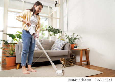Young asian woman using vacuum cleaner machine to cleaning carpet and floor in living room at home in the weekend morning. Living lifestyle at home. Young asian woman using vacuum cleaner machine to cleaning carpet and floor in living room at home in the weekend morning. Living lifestyle at home. 107208031