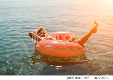 Summer vacation woman in hat floats on an inflatable donut mattress. Happy woman relaxing and enjoying family summer travel holidays travel on the sea. 107208570