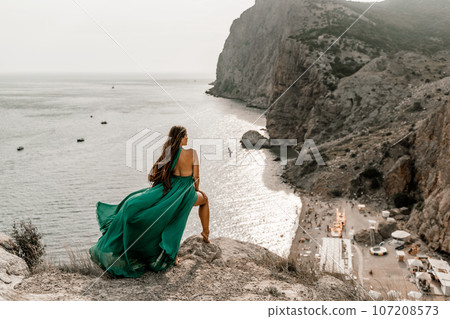 Woman sea green dress. Side view a happy woman with long hair in a long mint dress posing on a beach with calm sea bokeh lights on sunny day. Girl on the nature on blue sky background. 107208573