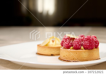 French patisserie. Still life with a delicious tartlet and raspberries with lemon on a white plate French patisserie. Still life with a delicious tartlet and raspberries with lemon on a white plate 107212021