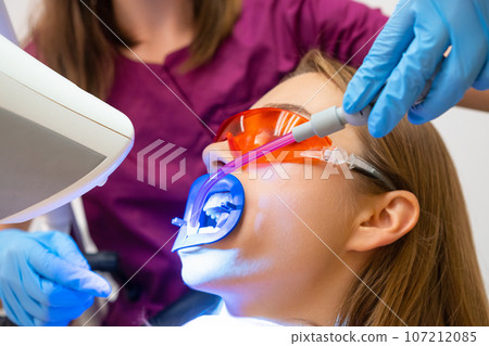 A dentist utilizing a saliva ejector during the teeth whitening treatment for a young patient. 107212085