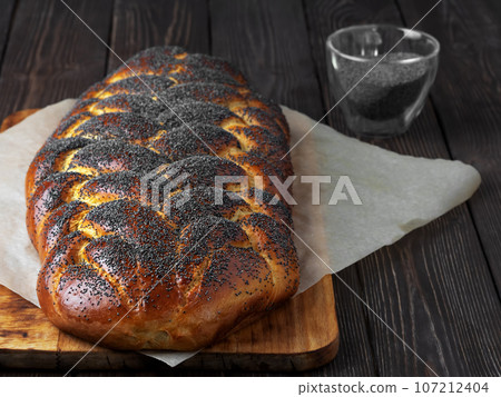 freshly baked sweet braided bread ( challah bread) with poppy seeds on a dark wooden background. Close-up, shallow depth of field. 107212404