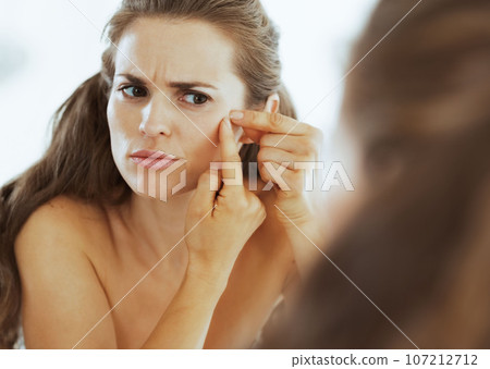 Frustrated young woman squeezing acne Frustrated young woman squeezing acne 107212712