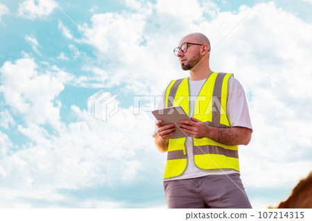 Clear air. Bottom view of bald bearded man with glasses holding tablet against blue cloudy sky. Copy space. Concept of environmental protection and recycling industry 107214315