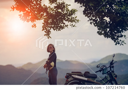woman holding safety helmet standing beside enduro motorcycle against beautiful mountain scene of khaoyai national park thailand 107214760