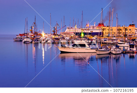 View of port area and bay in Heraklion, capital of Crete island, Greece. Ferries and cruises, fishing boats moored in harbor at sunset. Clear blue sky, deep blue waters, yachts, sailboats. Travel 107216195