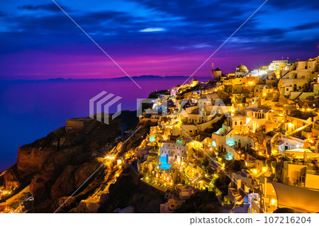 Beautiful view of Oia village with traditional whitewashed houses and windmills, Santorini island, at sunset, Greece. Scenic travel background, famous destination, colorful sky and clouds. Beautiful view of Oia village with traditional whitewashed houses and windmills, Santorini island, at sunset, Greece. Scenic travel background, famous destination, colorful sky and clouds. 107216204