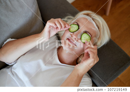 Blonde woman with a fabric mask on her face and cucumber slices on her eyes Blonde woman with a fabric mask on her face and cucumber slices on her eyes 107219149