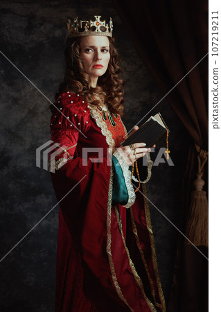 medieval queen in red dress with book, rosary and crown 107219211