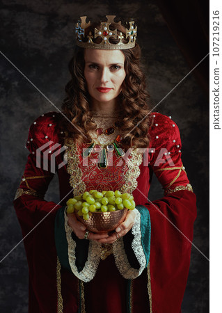 medieval queen in red dress with plate of grapes and crown 107219216